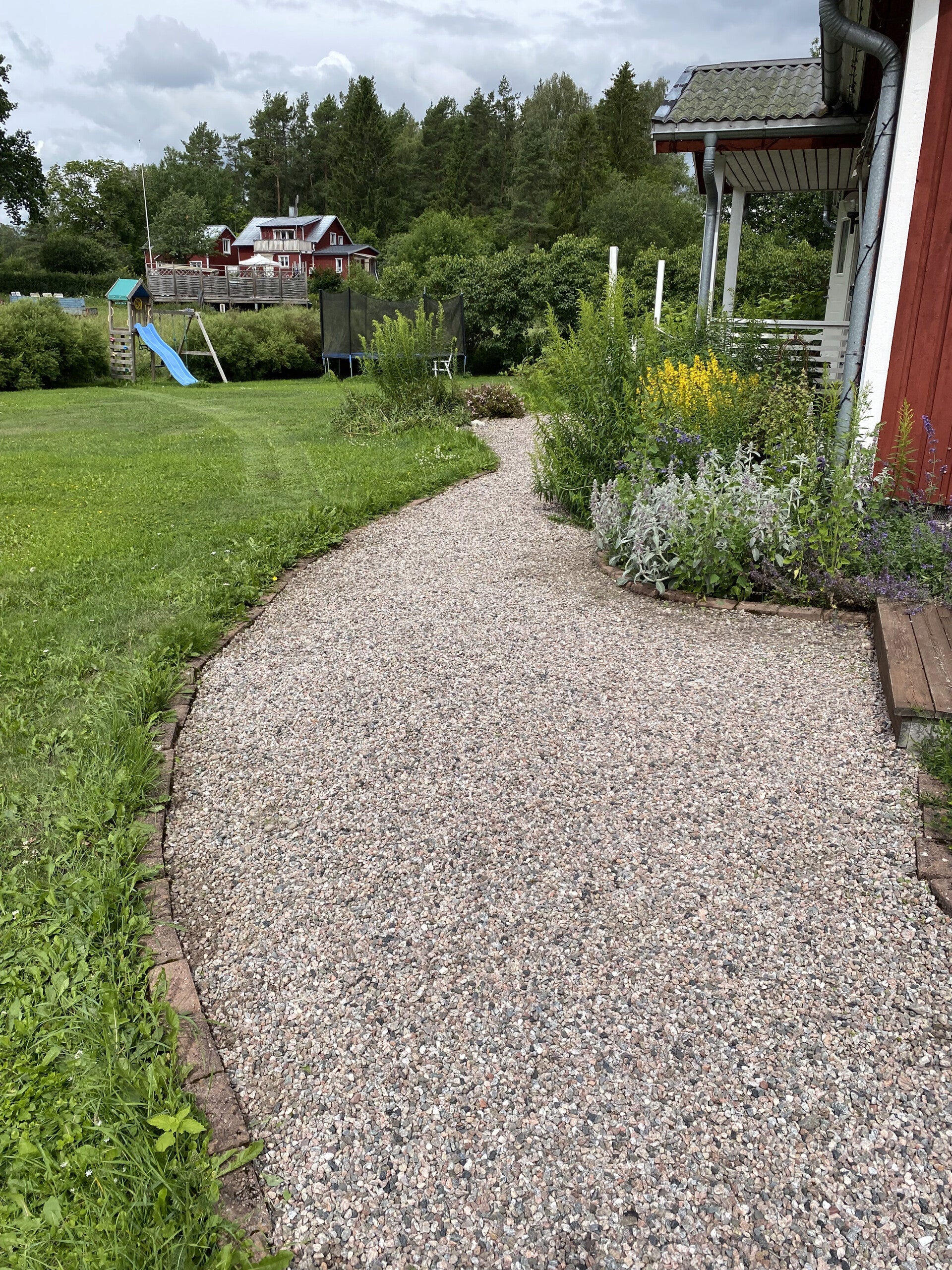 Grusgång och rabatt längs ett rött hus